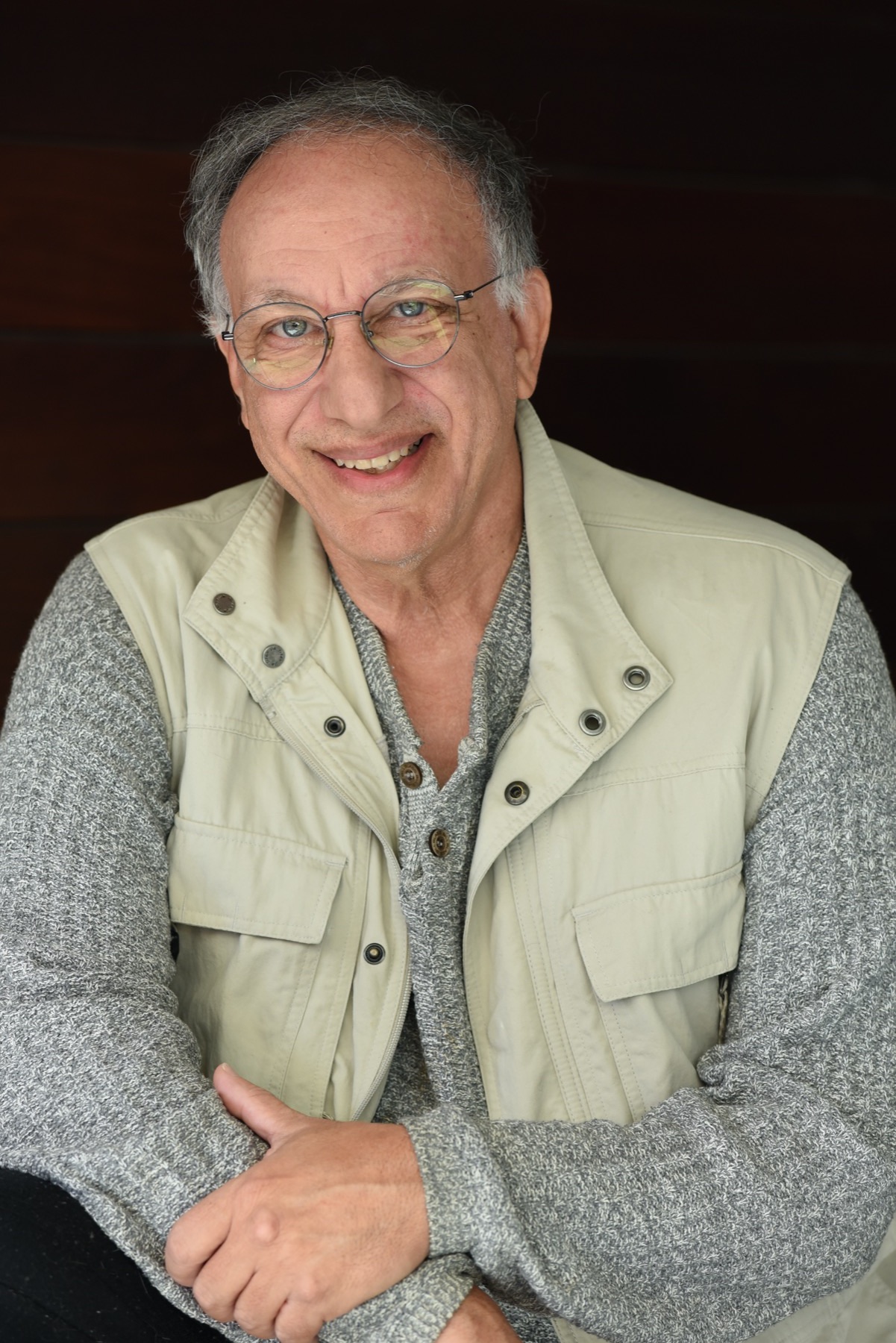 Smiling filmmaker Ted Faye wearing round glasses and a beige utility vest